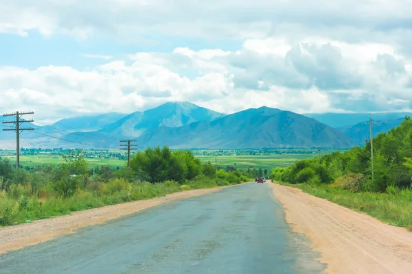 前往吉尔吉斯斯坦的公路旅行 群山对多云的天空 路边的绿色树木和灌木 — 图库照片