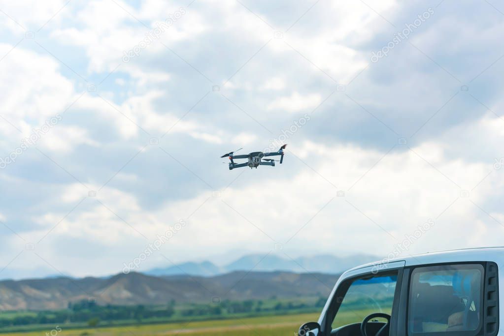 Copter for video flying over a white car. Rest in Kyrgyzstan. Shooting nature Issyk Kul from a bird's eye view.