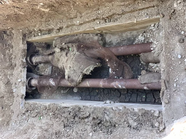 Replacement of heating pipes. Repair of pipes with drinking water. The texture of excavated earth. Metal pipe under the ground.