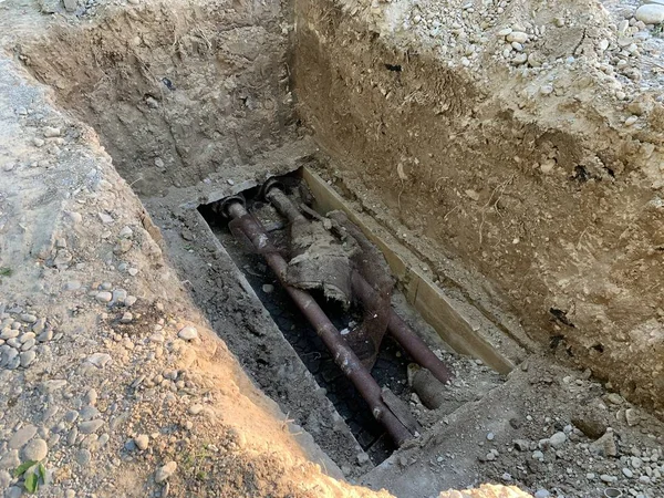 Replacement of heating pipes. Repair of pipes with drinking water. The texture of excavated earth. Metal pipe under the ground.