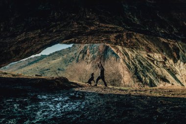 Mağarada köpeği olan bir adam. Dağlarda yürüyen bir rottweiler'ı olan bir adam. Bir adam köpeğiyle dışarıda oynuyor.