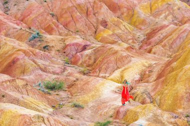 Kırgızistan'daki kanyon peri masalında kırmızı elbiseli kız. Kırgızistan'ın İsyk-Kul bölgesinin turuncu-sarı-kırmızı dağlarında bir kadın. Çok renkli dağların arka planda güzel kız. Orta Asya'da çok renkli kayalıklar.