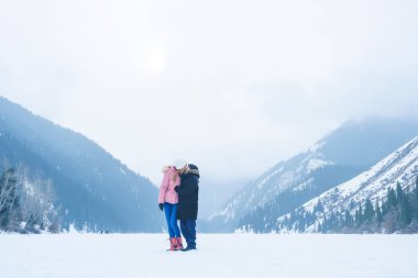Almat bölgesindeki donmuş Kolsay Gölü'ndeki kız ve adam. Genç çift kışın dağlarda tatilde. Kışın Kolsai Gölü. Orta Asya'da Kazakistan dağlarında yürüyüş turizmi.