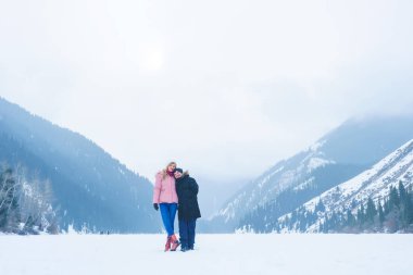 Almat bölgesindeki donmuş Kolsay Gölü'ndeki kız ve adam. Genç çift kışın dağlarda tatilde. Kışın Kolsai Gölü. Orta Asya'da Kazakistan dağlarında yürüyüş turizmi.