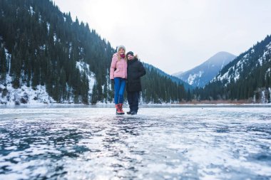 Almat bölgesindeki donmuş Kolsay Gölü'ndeki kız ve adam. Genç çift kışın dağlarda tatilde. Kışın Kolsai Gölü. Orta Asya'da Kazakistan dağlarında yürüyüş turizmi.