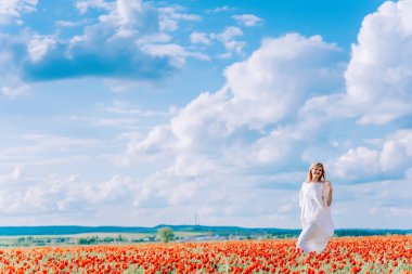 Haşhaş tarlasında beyaz elbiseli bir kız. Kırmızı çiçeklerle tarlada genç bir kadın. Büyük beyaz bulutların arka planında haşhaş tarlasında bir kız.
