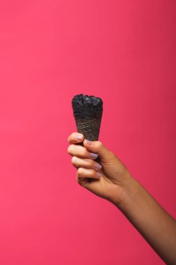 Pembe arka plan daki waffle konisinde siyah dondurma. Bir kadın elinde kömür dondurma boynuzu. Renkli bir arka plan üzerinde soğuk tatlı.