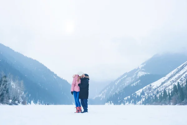 The girl and the guy on the frozen lake Kolsay in Almaty region. Young couple on vacation in the mountains in winter. Lake Kolsai in winter. Hiking tourism in the mountains of Kazakhstan in Central Asia.