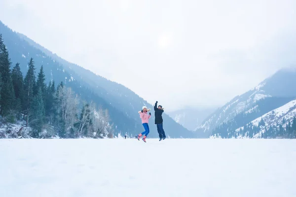 The girl and the guy on the frozen lake Kolsay in Almaty region. Young couple on vacation in the mountains in winter. Lake Kolsai in winter. Hiking tourism in the mountains of Kazakhstan in Central Asia.