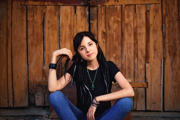 Ahşap arka planda siyah beyaz dreadlocks ile kız. Doğal dreadlocks ile kadın. Köyde ahşap kapı yakınında oturan güzel beyaz kız.