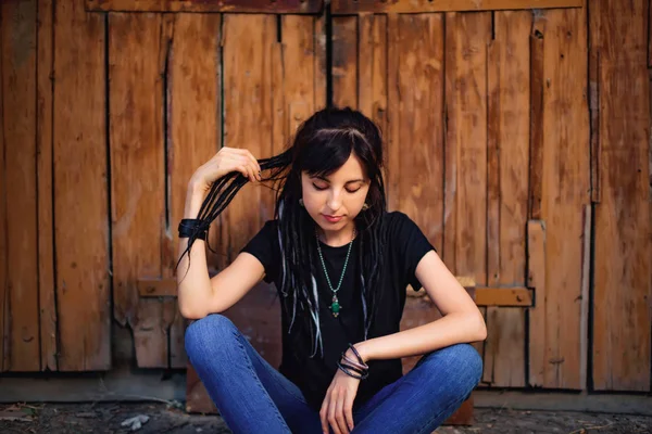 Ahşap arka planda siyah beyaz dreadlocks ile kız. Doğal dreadlocks ile kadın. Köyde ahşap kapı yakınında oturan güzel beyaz kız.