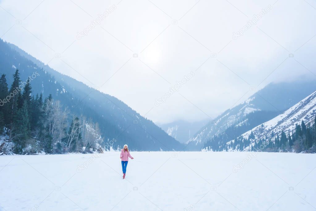 Girl in the mountains in winter on a frozen lake. Tourist girl on winter lake Kolsay in the mountains in Kazakhstan. Mountain lake Kolsay in the Almaty region.