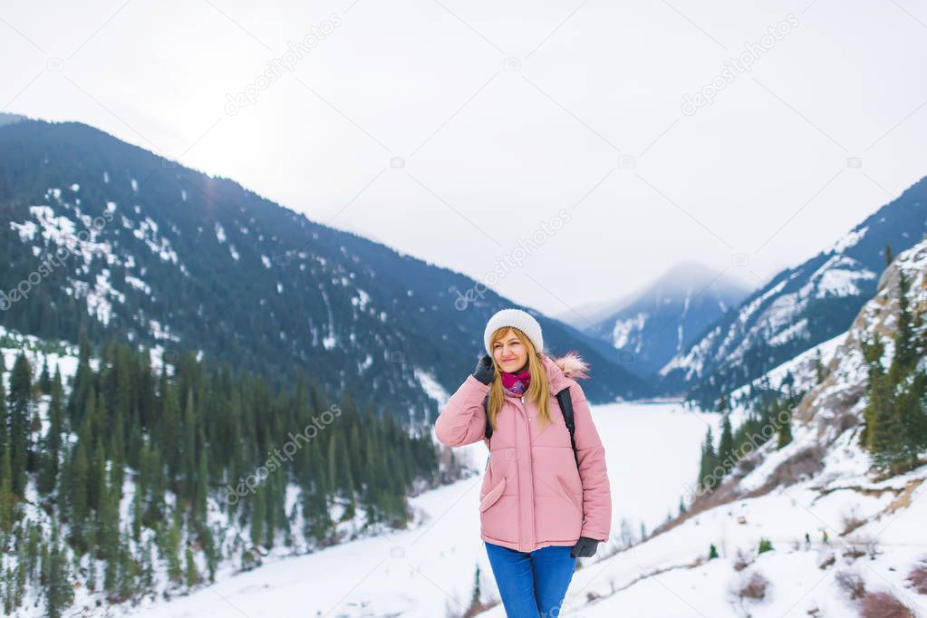 Girl in the mountains in winter on a frozen lake. Tourist girl on winter lake Kolsay in the mountains in Kazakhstan. Mountain lake Kolsay in the Almaty region.