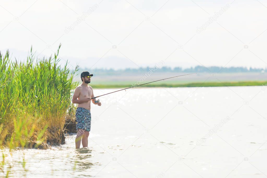 A man with a fishing rod in the reeds on the lake. The guy is fishing from the riverbank. Summer fishing on the lake Issyk Kul