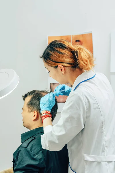 A young man with a bald spot in the office of a trichologist cosmetologist. Mesotherapy of hair and head. Fighting hair loss in men. Injections to the head as a fight against baldness in men