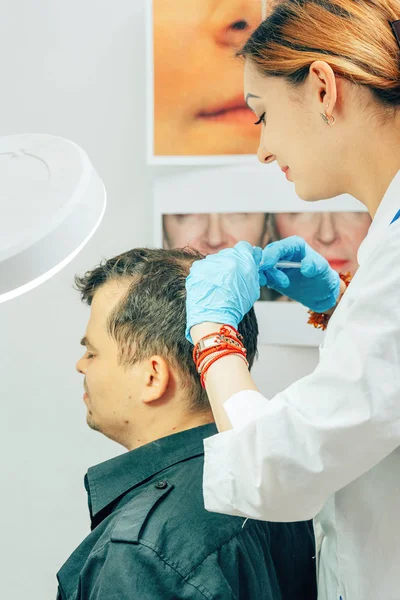 A young man with a bald spot in the office of a trichologist cosmetologist. Mesotherapy of hair and head. Fighting hair loss in men. Injections to the head as a fight against baldness in men