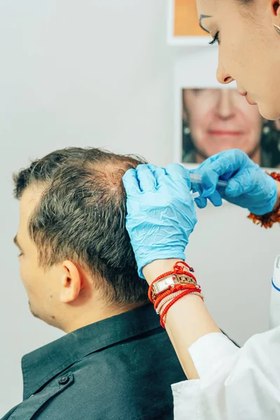 A young man with a bald spot in the office of a trichologist cosmetologist. Mesotherapy of hair and head. Fighting hair loss in men. Injections to the head as a fight against baldness in men