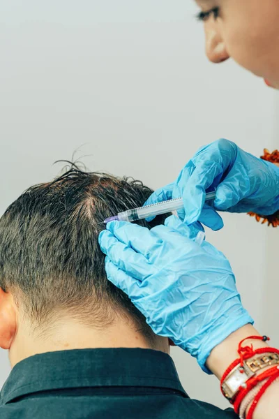 Mesotherapy of hair and head. Injections in the head. Male pattern baldness. Fighting hair loss in men. Men\'s bald spot in the center of the head at the crown. The hands of the cosmetologist the doctor of the trichologist and the head of the patient