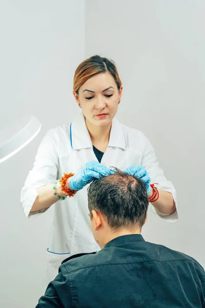 A young man with a bald spot in the office of a trichologist cosmetologist. Preparing for mesotherapy of hair and head. Fighting hair loss in men. Treatment methods for male pattern baldness