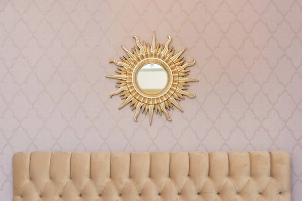 The mirror in the frame in the form of the sun in the living room on the wall. Mirror in a gold frame. Beauty mirror in the interior.