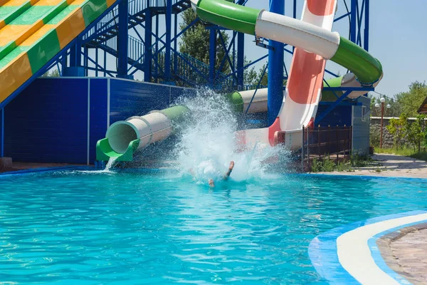 The guy rolled down the slide at the water Park. Splashes of water in the pool. Summer vacation in the water Park.