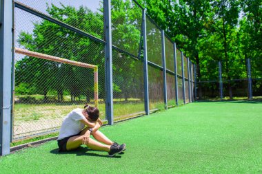 Kız eğitimden sonra dinleniyor. Çocuklar oyun alanında topla oynarlar. Futbol sahasında ısınma sporcusu.
