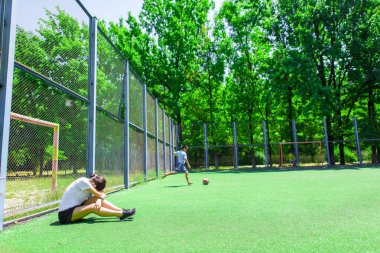 Kız eğitimden sonra dinleniyor. Çocuklar oyun alanında topla oynarlar. Futbol sahasında ısınma sporcusu.