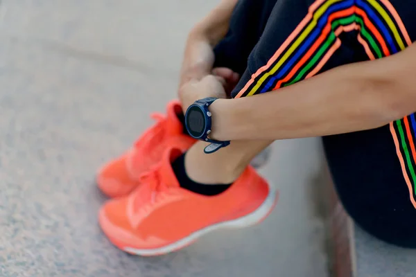 Sports shoes orange. Fitness watch on the girl\'s hand. Athlete resting after training.