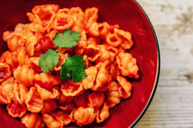 Beyaz ahşap bir masa üzerinde bordo plaka domates soslu Makarna. Makarna domates ile kabukları şeklinde. Öğle yemeği için ev yapımı makarna