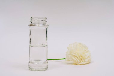 White ranunculus near vase. Flower and vase on a white background. One flower lies near a jar of water.