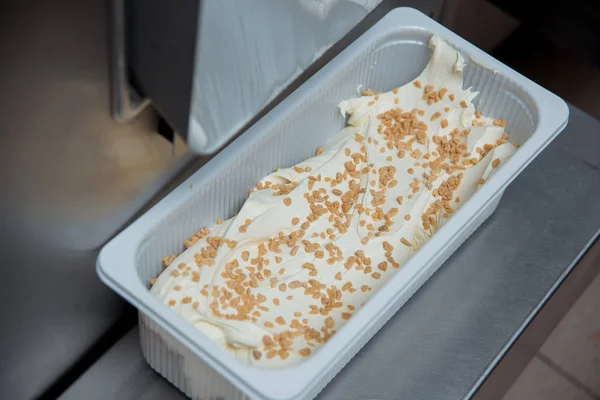 Preparation of ice cream at a candy factory. Sweet dessert. Ice cream in a container sprinkled with crispy balls.