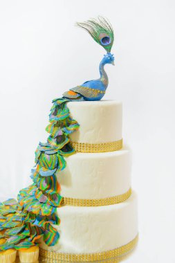 Üç katlı beyaz kek. Bir kuş tavuskuşu figürü ile süslenmiş tatlı pasta. Beyaz buzlanma içinde pasta stand üzerinde.