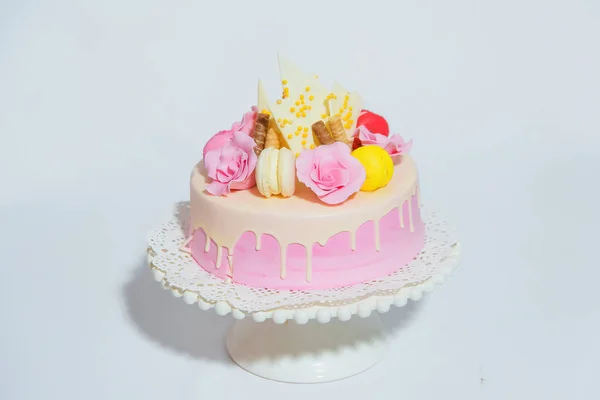 Pink cake on white background. Sweet pastry decorated with pieces of chocolate and colored macaroons Cake in pink glaze is on the stand.