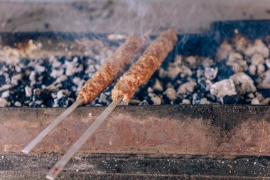 Izgarada kıyma nın şişleri kavuruyor. Bir tabak kızarmış et. Yanan kömürler ve duman.