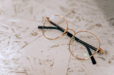 Yuvarlak gözlükler beyaz bir masanın üzerinde yatıyor. Gözlük üzerinde altın kaplama jant.