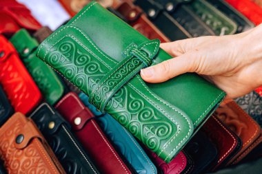 Ulusal Kazak süsü ile deri cüzdan. Kazakistan'da hakiki deriden yapılmış aksesuarlar. Çimkent şehrinde Arbat caddesi boyunca yürüyün. Kızın elindeki yeşil çanta..