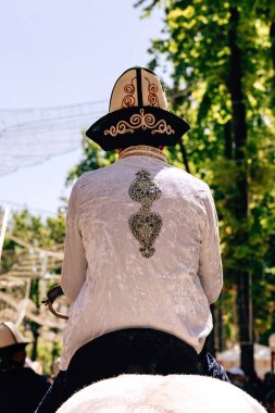 Kazak milli elbisesi olan bir adam ata biniyor. Çimkent şehrinde Arbat caddesi boyunca yürüyün. Kazakistan'da çiçek festivali.