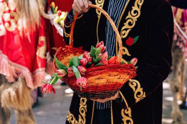 Kazak milli elbisesi içinde bir adam elinde lale sepeti tutuyor. Çimkent şehrinde Arbat caddesi boyunca yürüyün. Kazakistan'da çiçek festivali.