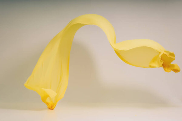 Yellow fabric on a white background. Levitate yellow fabric in the photo studio. A soaring piece of cotton fabric. Flying colored fabric on a light background