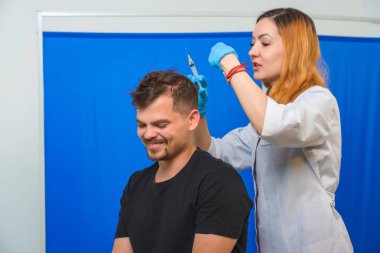 Doktorun ofisindeki kanepedeki adam. Genç bir adam için mezoterapi. Kafasına şırınga yla iğneler. Saç uzatma kel adam. Fotoğraf stüdyosundaki tıp ofisi. Vitamin enjeksiyonları