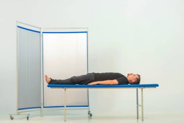 Doktordaki resepsiyondaki genç adam. Adam tıbbi kanepede yatıyor. Resepsiyondaki bir adam kozmetik uzmanı..