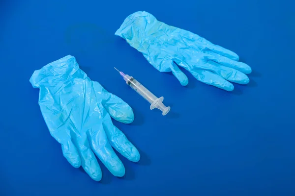 Blue gloves on a blue lounger. Medical gloves with a syringe. Dirty medical instrumentation after the procedure. Used syringe in the medical office