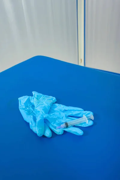 Blue gloves on a blue lounger. Medical gloves with a syringe. Dirty medical instrumentation after the procedure. Used syringe in the medical office