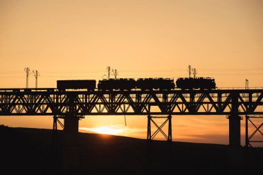 Kazakistan'da demiryolu köprüsü. Gün batımında yük treni. Orta Asya'da demiryolu kargo taşımacılığı. Köprü yapısı.