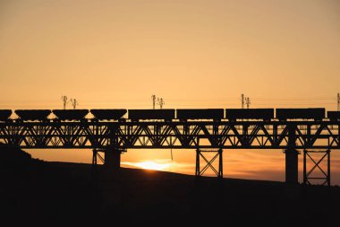 Kazakistan'da demiryolu köprüsü. Gün batımında yük treni. Orta Asya'da demiryolu kargo taşımacılığı. Köprü yapısı.