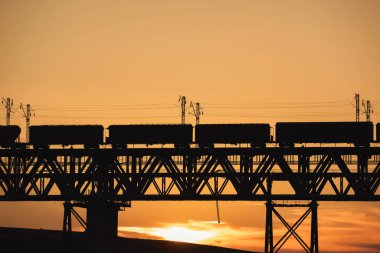 Kazakistan'da demiryolu köprüsü. Gün batımında yük treni. Orta Asya'da demiryolu kargo taşımacılığı. Köprü yapısı.
