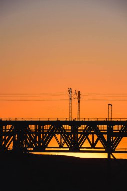Kazakistan'da demiryolu köprüsü. Turuncu bir gün batımının arka planında yük treni. Orta Asya'da demiryolu kargo taşımacılığı. Köprü yapısı.