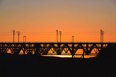 Kazakistan'da demiryolu köprüsü. Turuncu bir gün batımının arka planında yük treni. Orta Asya'da demiryolu kargo taşımacılığı. Köprü yapısı.