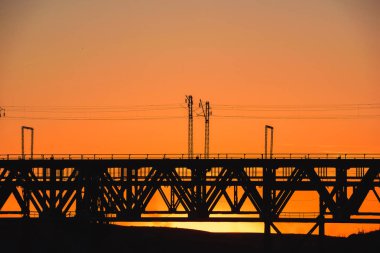 Kazakistan'da demiryolu köprüsü. Turuncu bir gün batımının arka planında yük treni. Orta Asya'da demiryolu kargo taşımacılığı. Köprü yapısı.