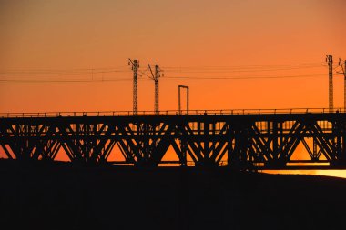 Kazakistan'da demiryolu köprüsü. Turuncu bir gün batımının arka planında yük treni. Orta Asya'da demiryolu kargo taşımacılığı. Köprü yapısı.